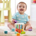 Baby boy sitting on a carpet in his playroom, smiling and playing with Montessori Shape Blocks.
