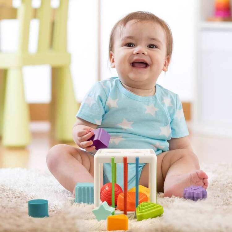 Baby boy sitting on a carpet in his playroom, smiling and playing with Montessori Shape Blocks.