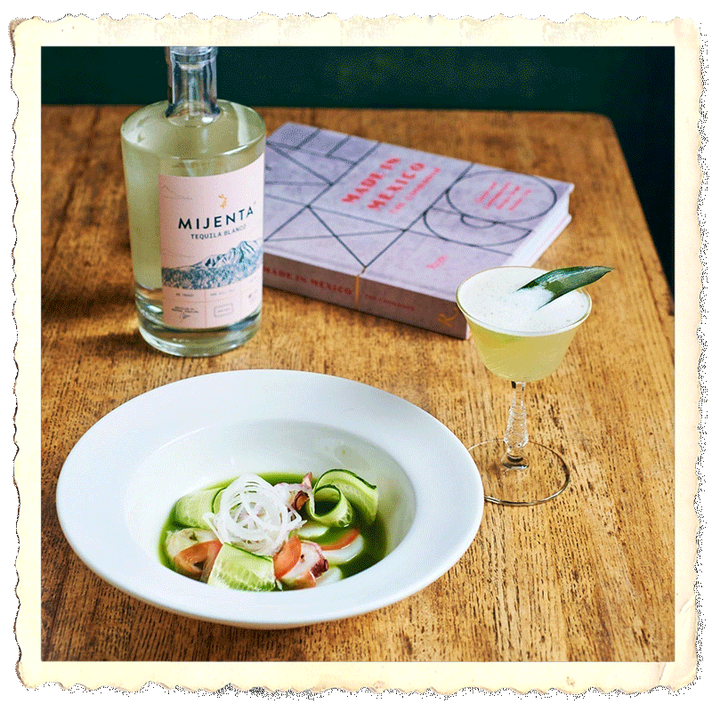 Aguachile verde dish in foreground, Mijenta Tequila Blanco bottle and book on wooden table