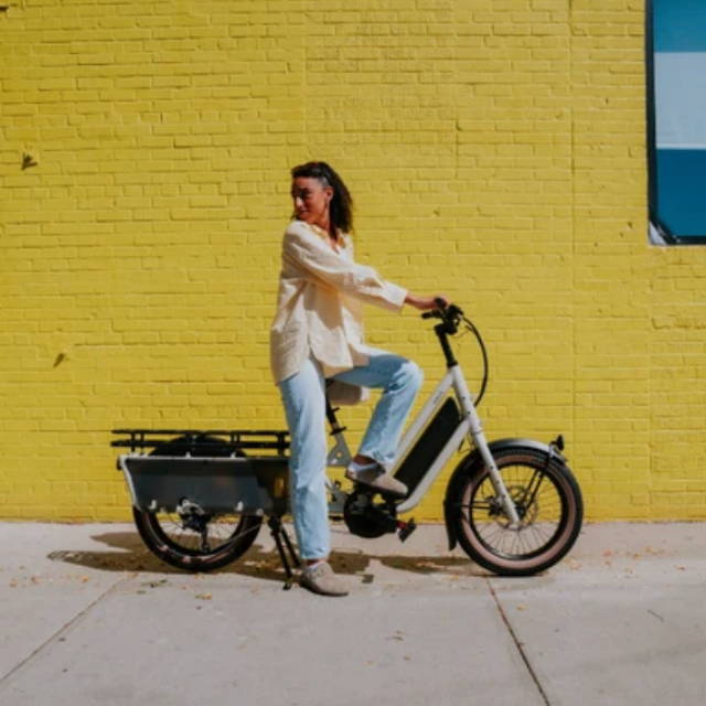a woman on a specialized electric cargo bike in front of a yellow brick wall