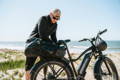 Un homme en train de remplir un sac de voyague sur son velo electrique a la plage