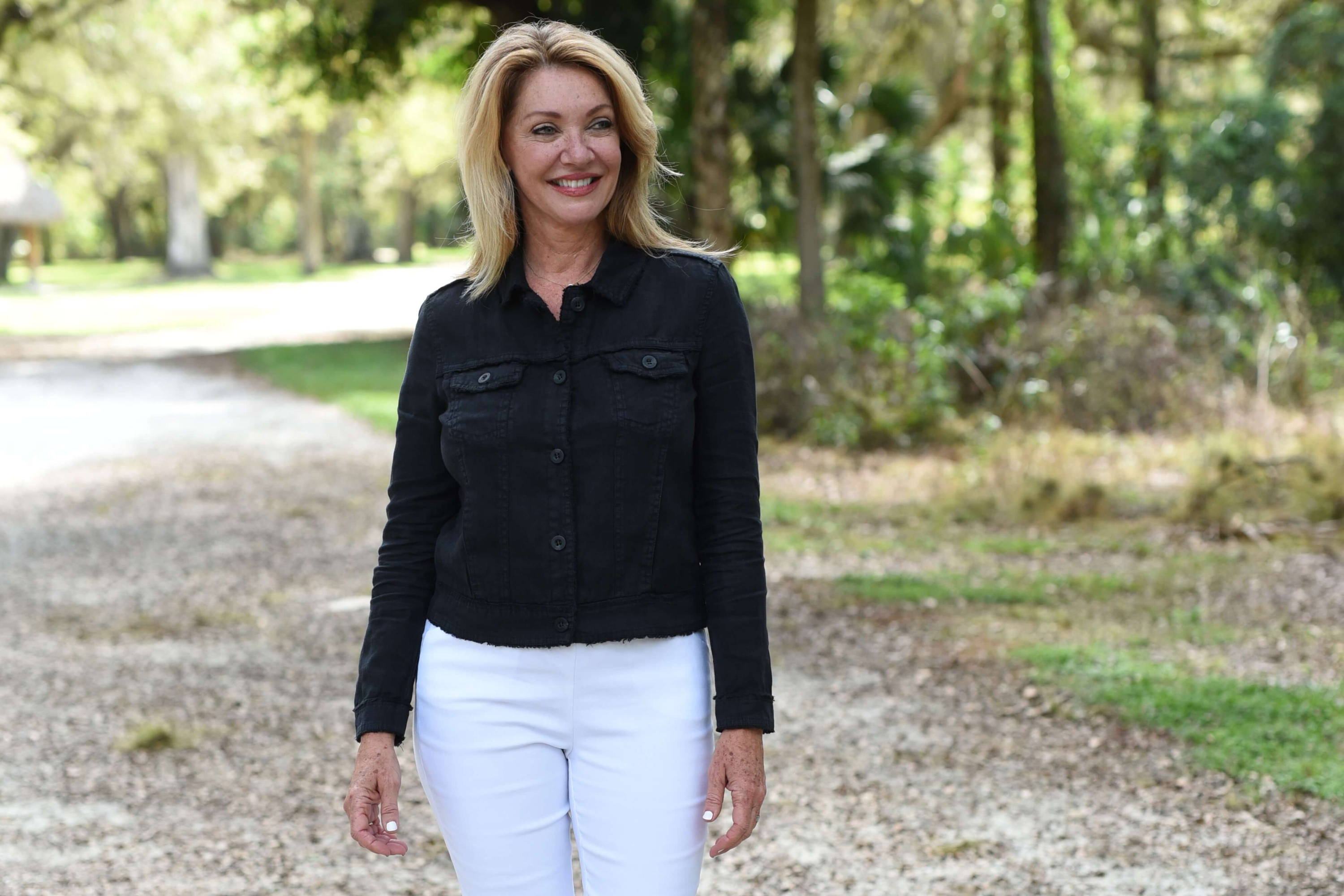 A woman wears a black top with white ankle pants in a sunny patch.