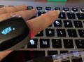 User holding Wellue O2Ring pulse oximeter over keyboard to monitor oxygen levels