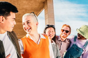 A group of multiracial attractive friends smile as they hold onto eachothers arms.