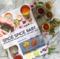 A book titled 'Spice Spice Baby' laying on a white granite countertop next to open glass spice jars