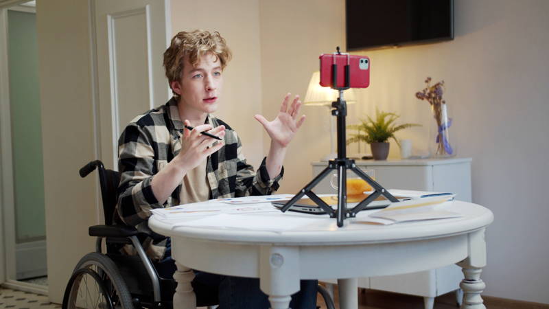 young male wheelchair user speaking to a phone on a tripod