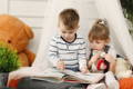 Brother and sister reading a book. 