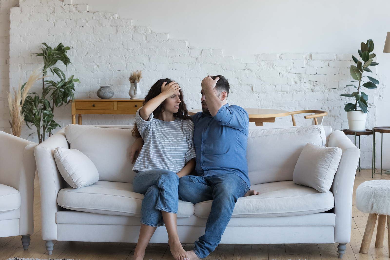 Couple sit on sofa put palms of foreheads look disappointed