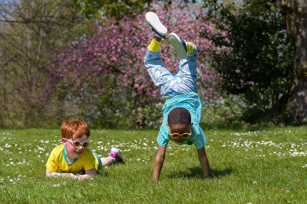 Image of two happy children playing in the park. One boy is doing a handstand. The other is lying in daisies. Both are wearing bright, colourful Ducky Zebra clothes