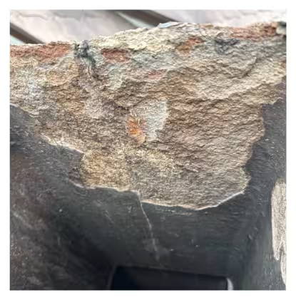 Close-up of a chimney crown with severe spalling and surface deterioration, exposing rough aggregate and cracking.