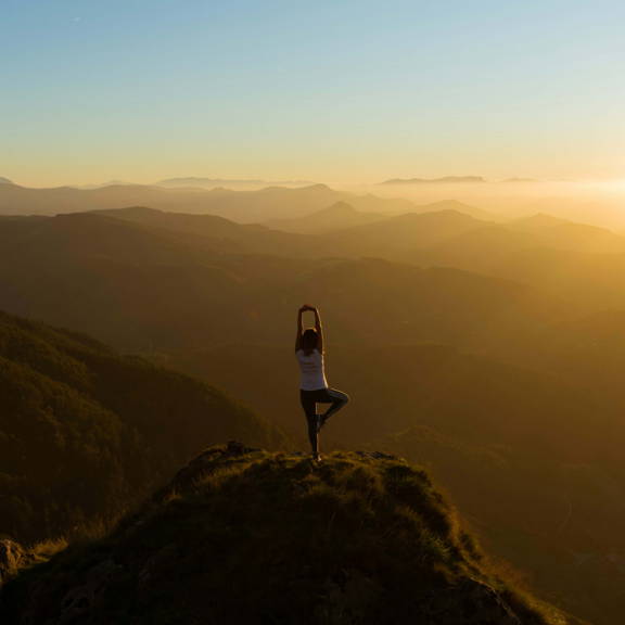 A women doing yoga at the top of a hill overlooking a sunset.