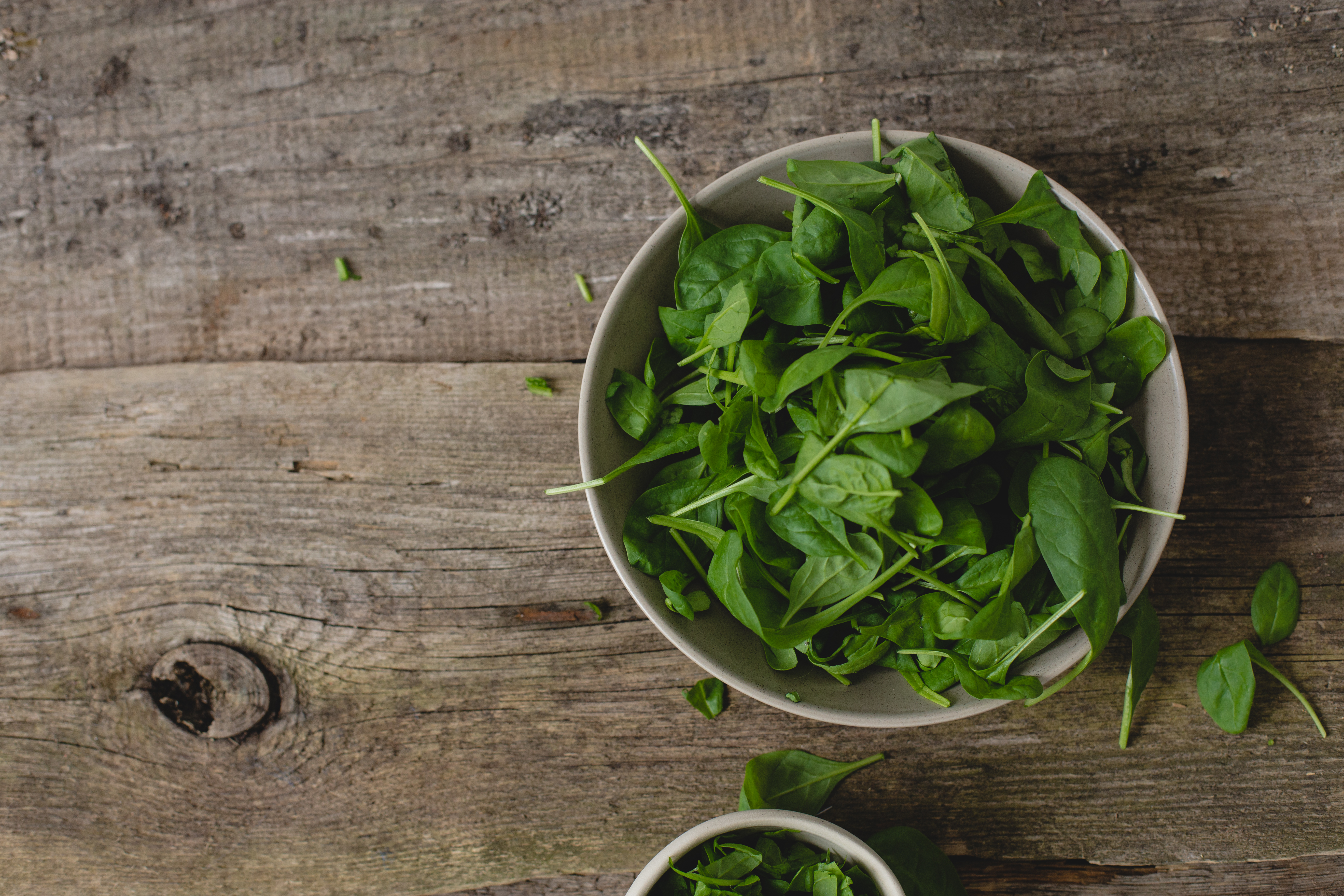 Baby spinach leaves in a white bowl on a wooden background