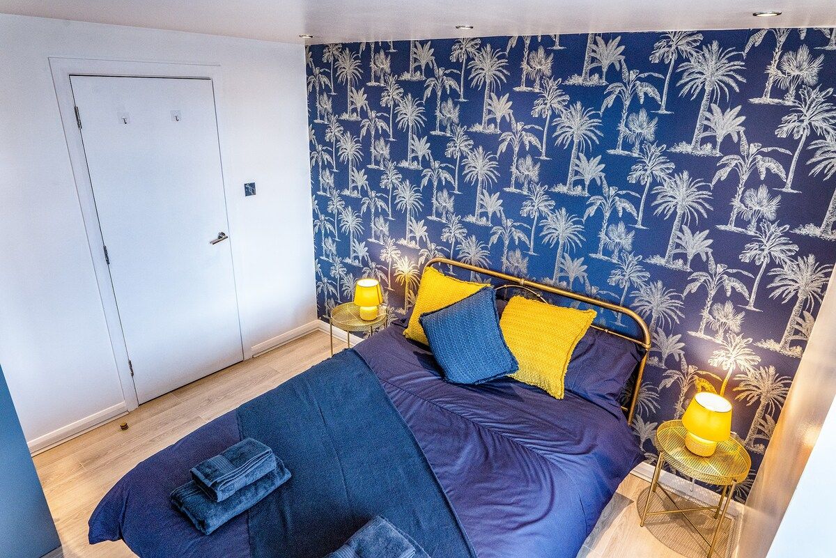 Bedroom showing double bed and patterned wallpaper with blue sheets and yellow accents