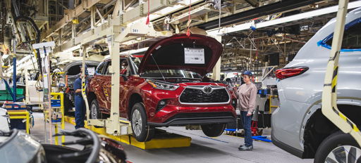 An automotive assembly line shows a red car being worked on amid busy workers and machinery, highlighting industry and teamwork.