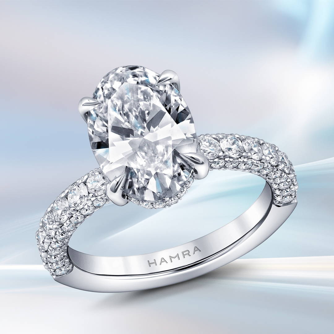 Oval shaped solitaire engagement ring with diamonds along the shank on a bluish background.
