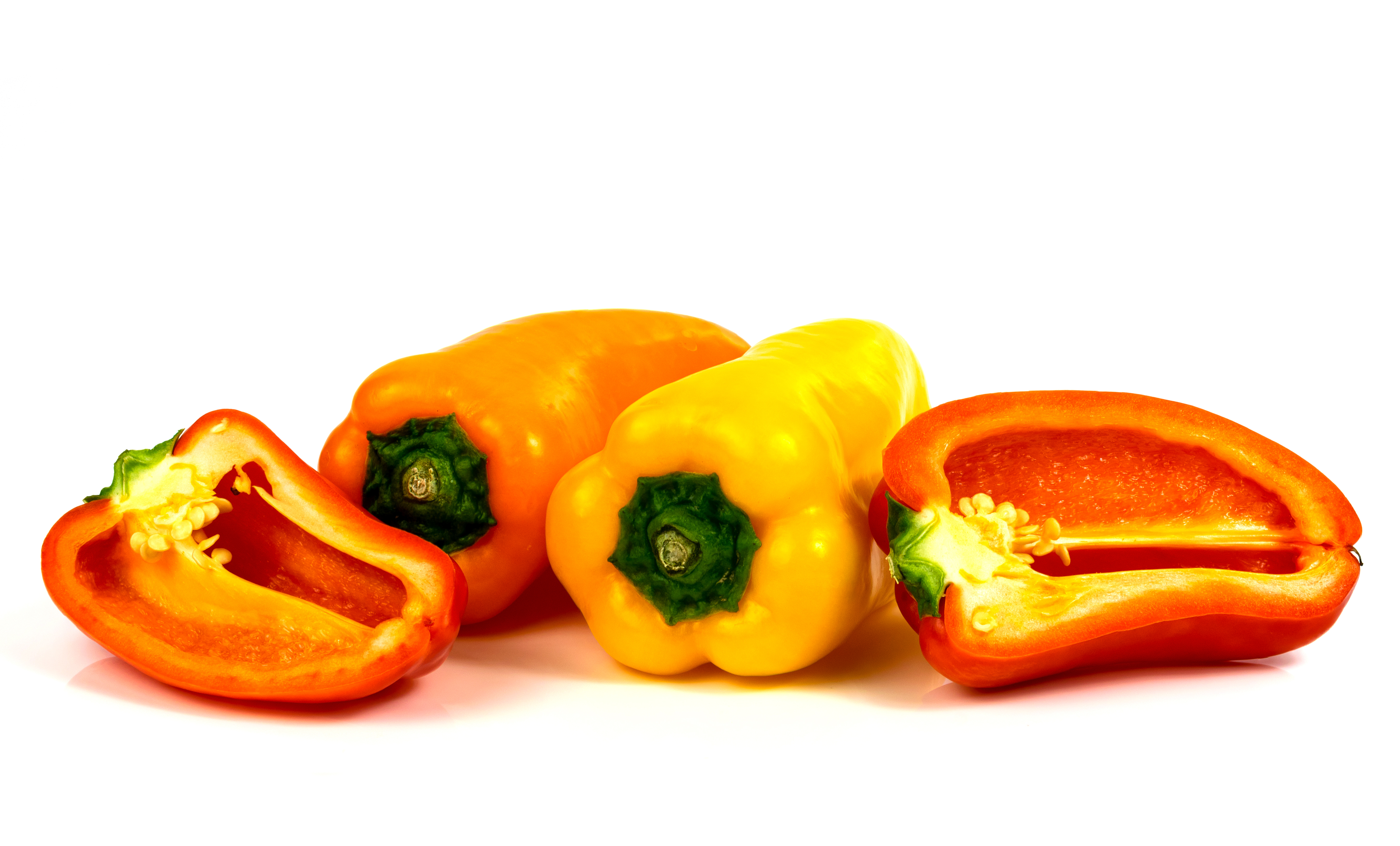 Orange, yellow, and red snack-sized peppers on a a white background. The red pepper is cut in half.