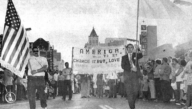 Black and white image of pride with people walking with american flags and a large banner.