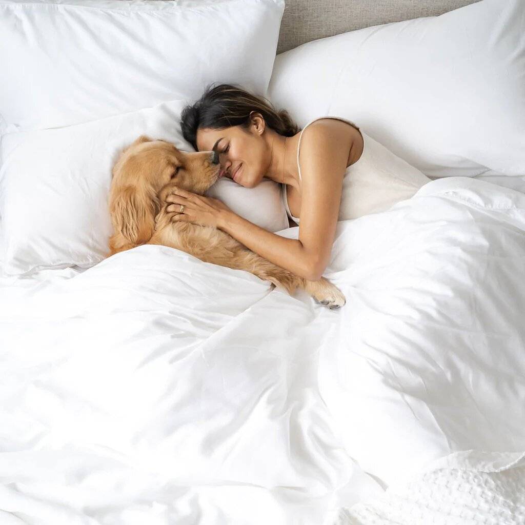 Woman lying on bed with pet featuring Weavve's white tencel bed sheets and cotton blanket