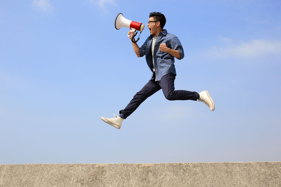 A man jumps high in the air with a megaphone yelling happily into the mic.