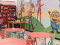 Buntes Kinderspielzimmer mit farbenfrohen Möbeln, Wandmalereien und Regalen voller Spielzeug.