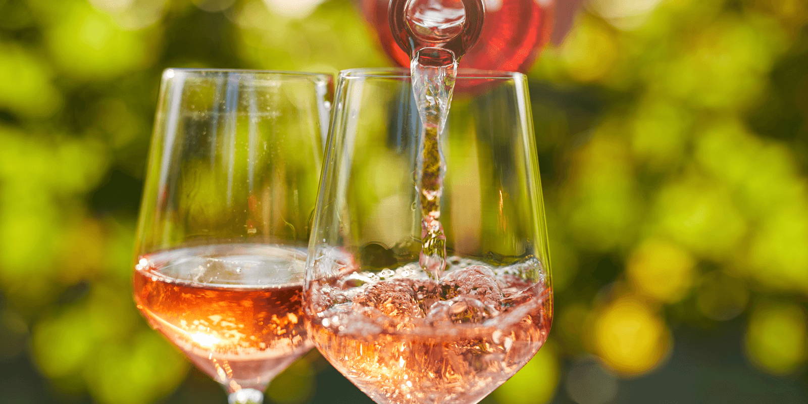 Close shot of two wine glasses, one filled and one being filled with orange wine.