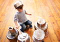 Toddler playing a homemade kitchen drum game with pots and wooden spoons on the floor at home.