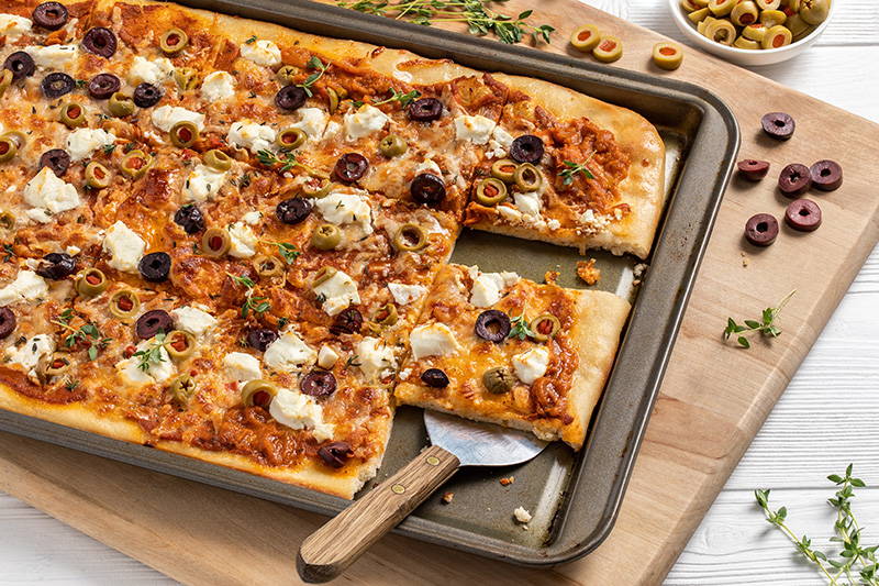 Spatula serving flatbread topped with olives.