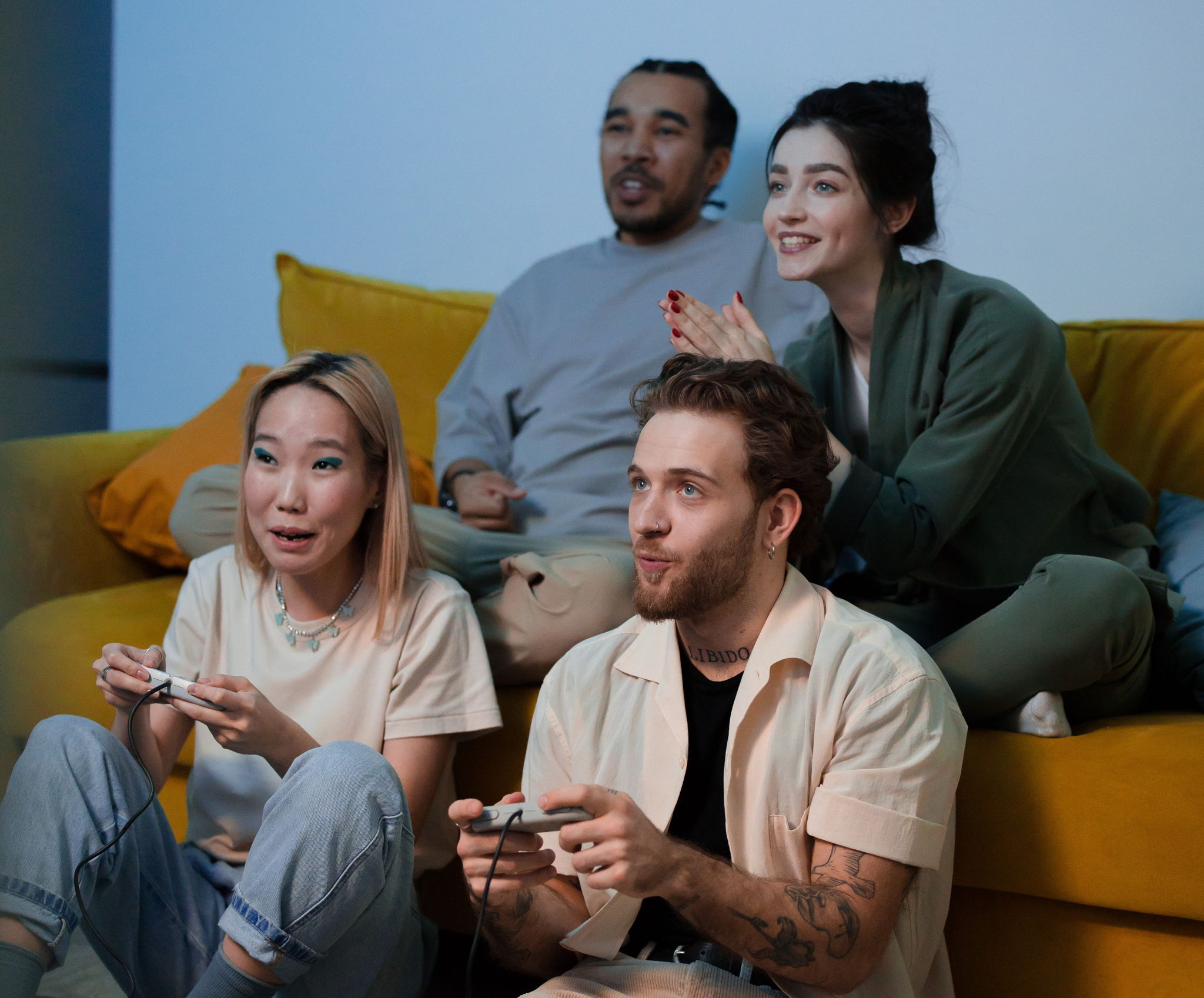 4 attractive multi ethnic friends, 2 men and 2 women, sitting and playing video games together laughing.