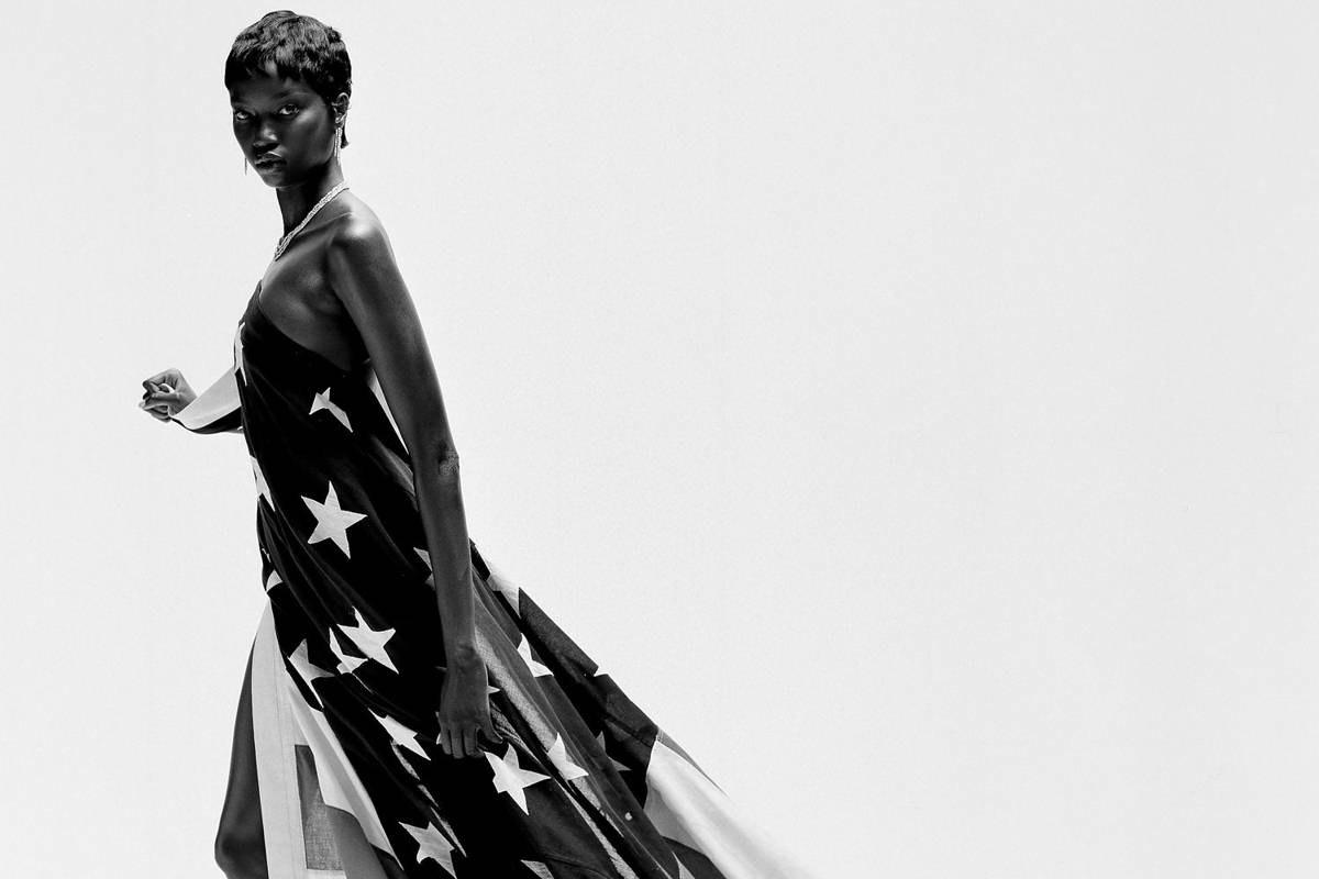A black and white image of supermodel Anok Yai, draped in an American flag and standing in front of a white background
