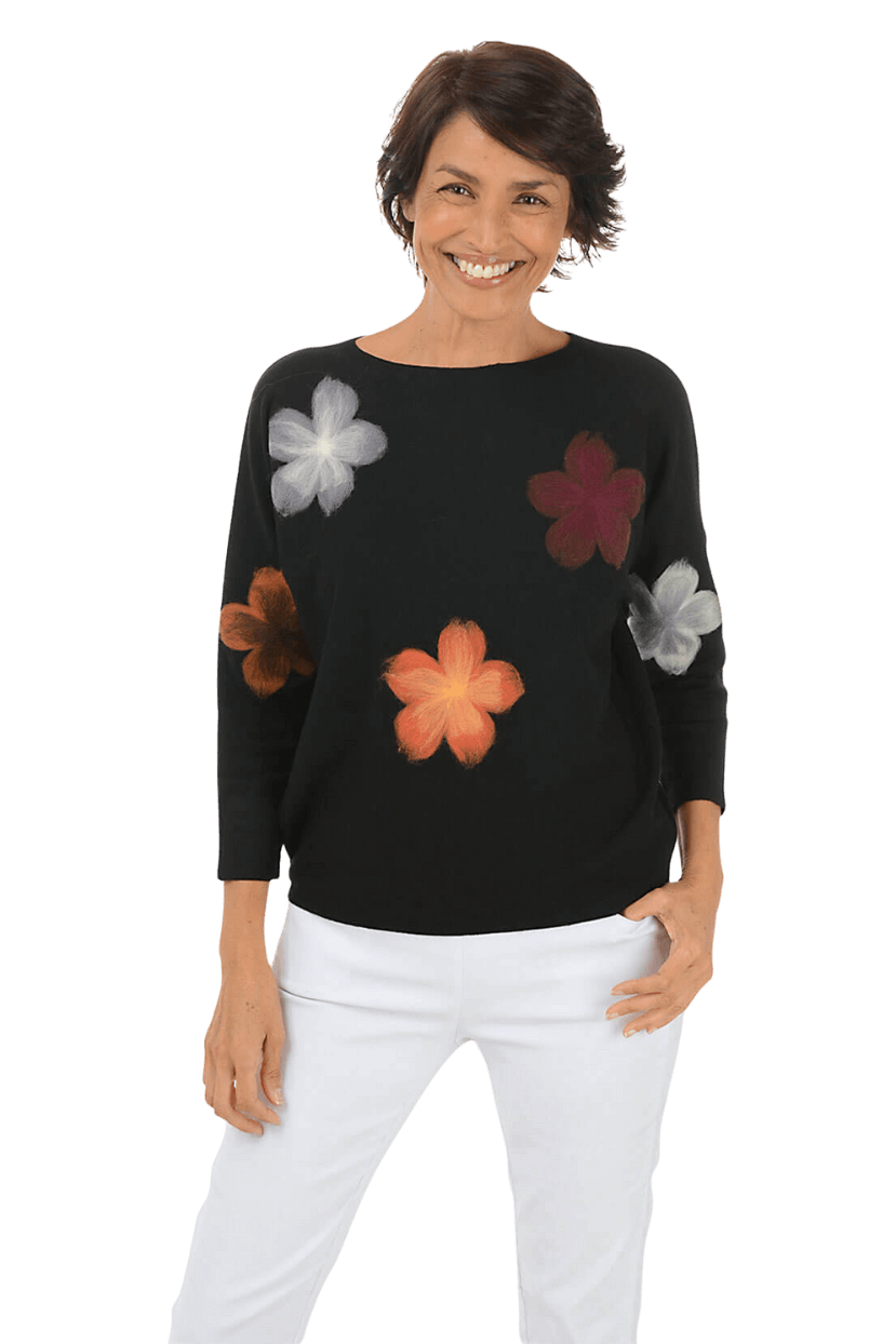 A woman wearing a black sweater with colorful flower details and white pants
