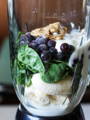 blender filled with ingredients: banana, spinach, blueberries, peanut butter and milk 