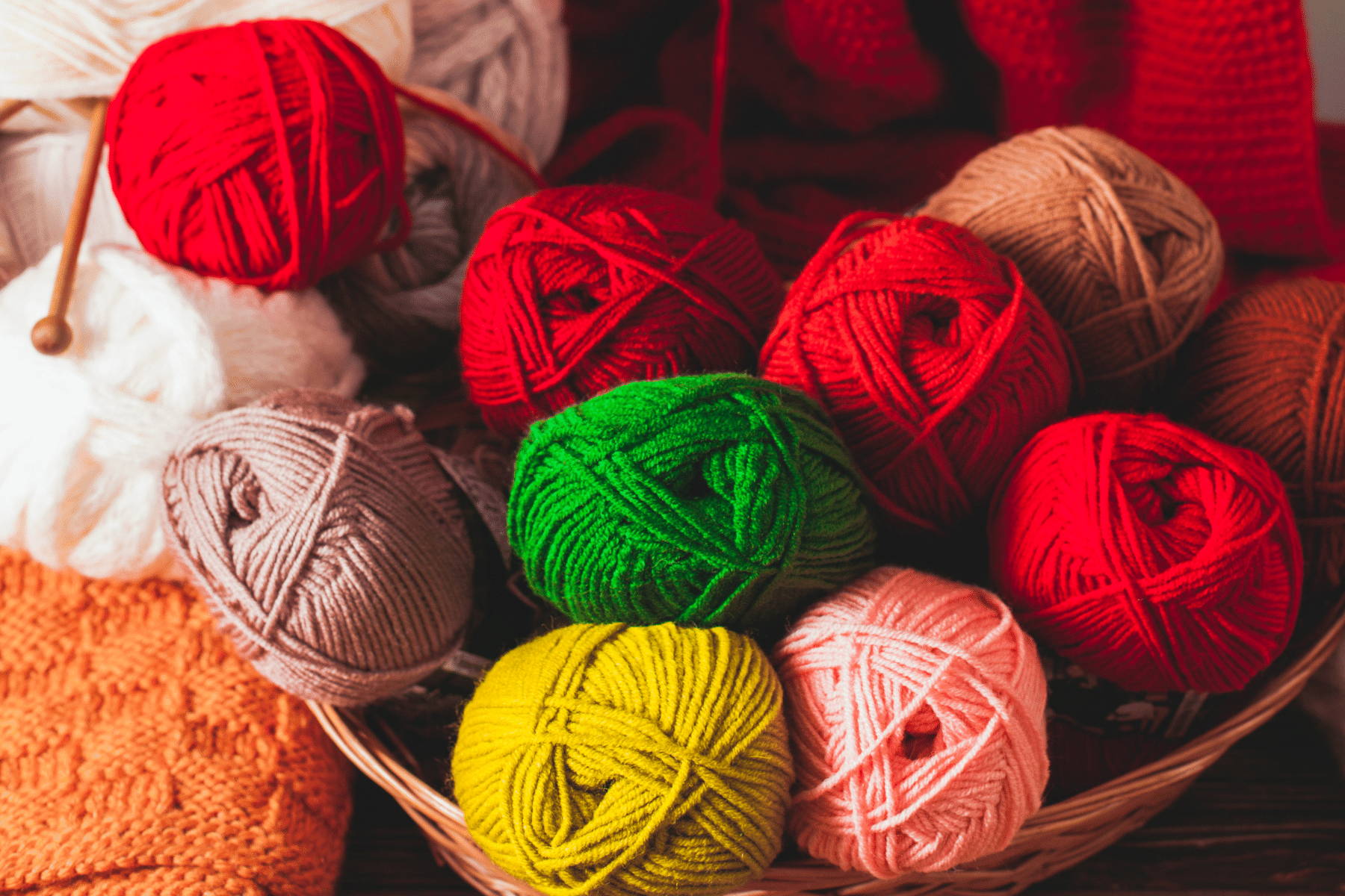 A wicker basket containing balls of yarns in brown, yellow, green, pink and red