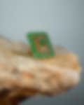 Exquisite rectangular gold ring adorned with vibrant green gemstones, resting on a stone surface against a muted backdrop.