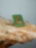 Exquisite rectangular gold ring adorned with vibrant green gemstones, resting on a stone surface against a muted backdrop.