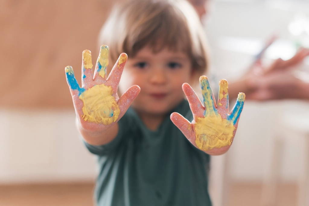 Toddler showing his messy hands after finger painting.