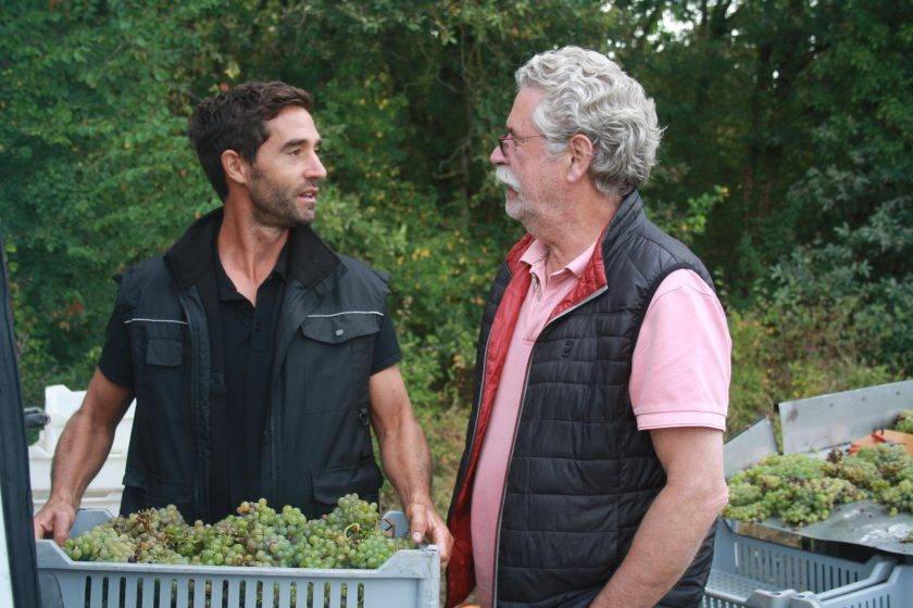 Jacky Blot et son fils Jean-Philippe Blot se tiennent côte à côte au Domaine de la Taille aux Loups. Jacky, le fondateur du domaine, sourit avec une fierté visible, tandis que Jean-Philippe, son successeur, partage son enthousiasme. En arrière-plan, on aperçoit les vignes verdoyantes et bien entretenues qui s'étendent sur les coteaux calcaires de Montlouis-sur-Loire, symbolisant le travail acharné et la passion familiale pour la viticulture.
