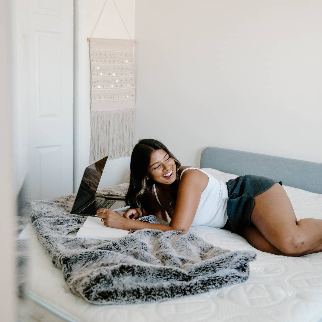 woman laying on bed with laptop and note pad laughing