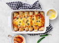 A white dish is filled with enchiladas with melted cheese and jalapenos