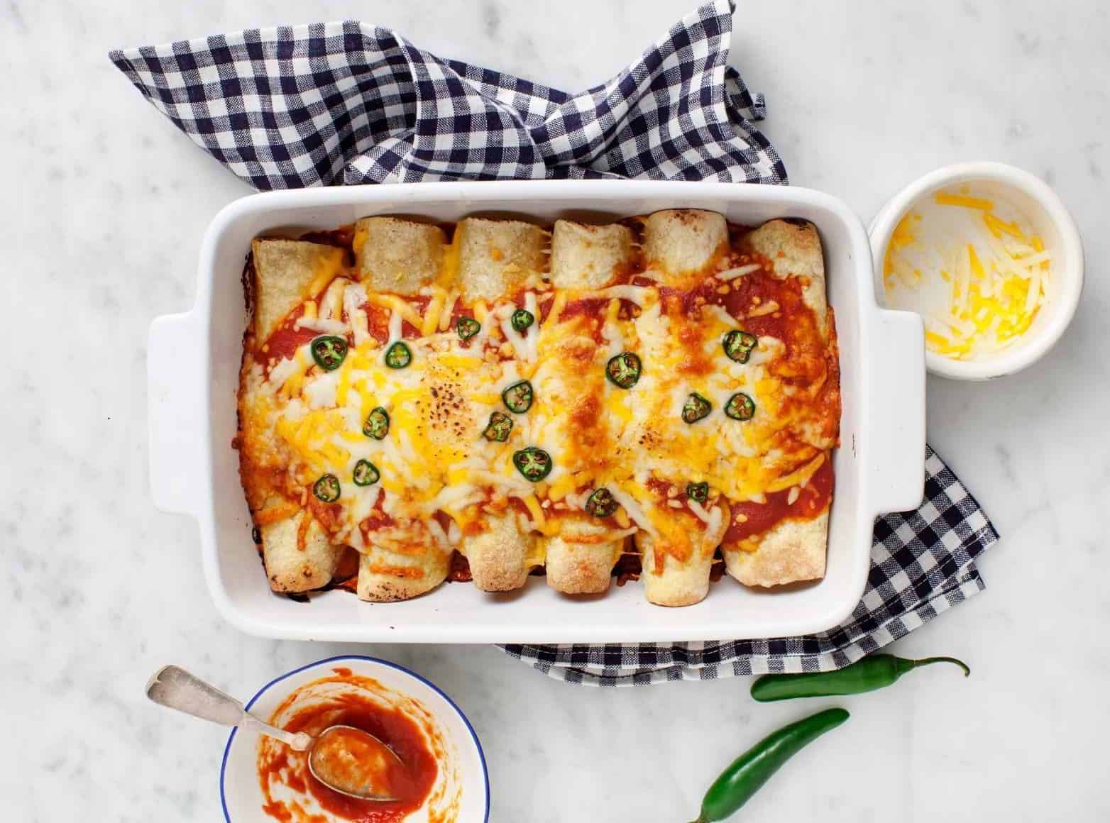 A white dish is filled with enchiladas with melted cheese and jalapenos