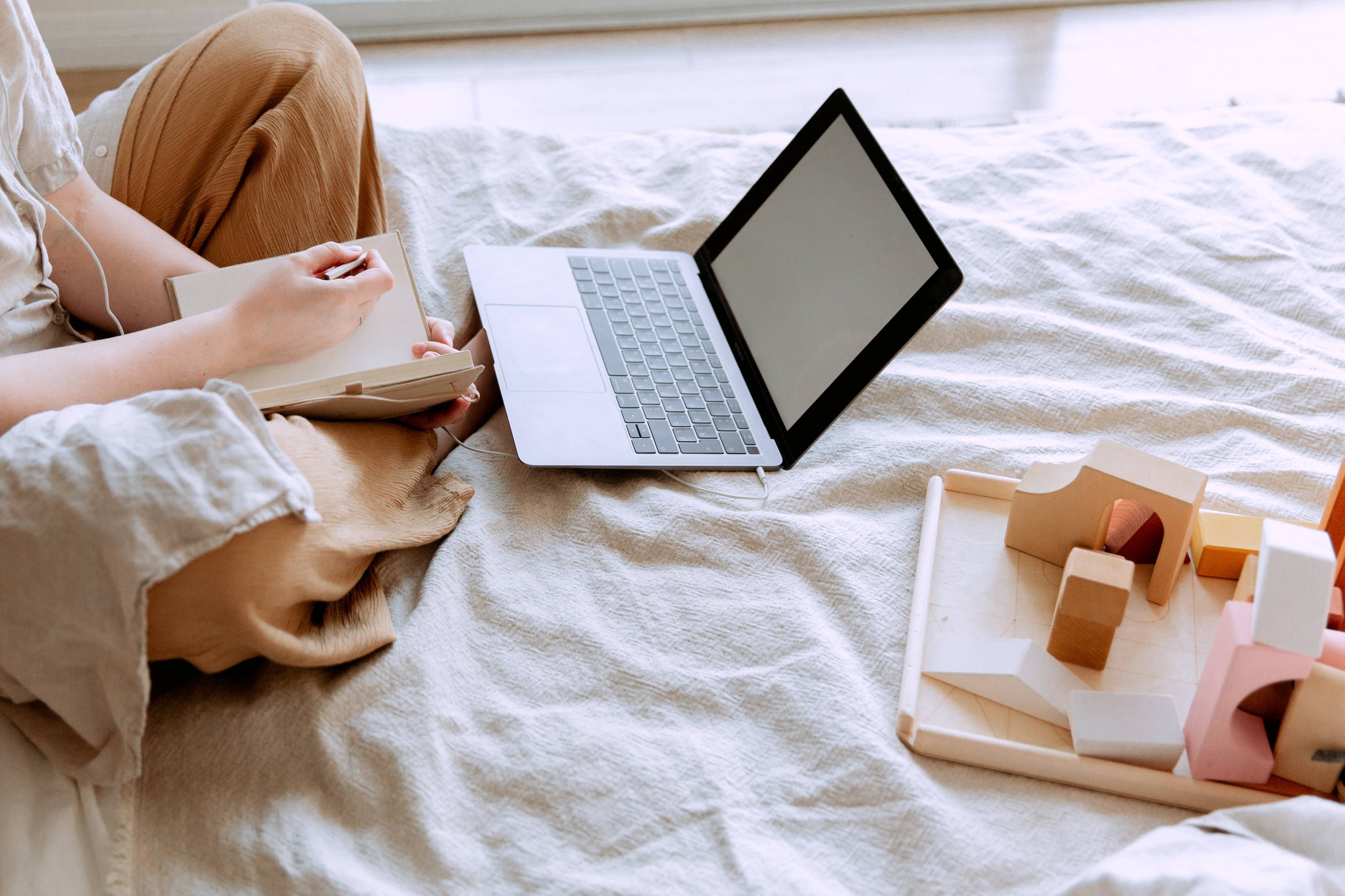 Woman sitting on her bed with a laptop and notebook doing wine research for upcoming dinner reservation..  