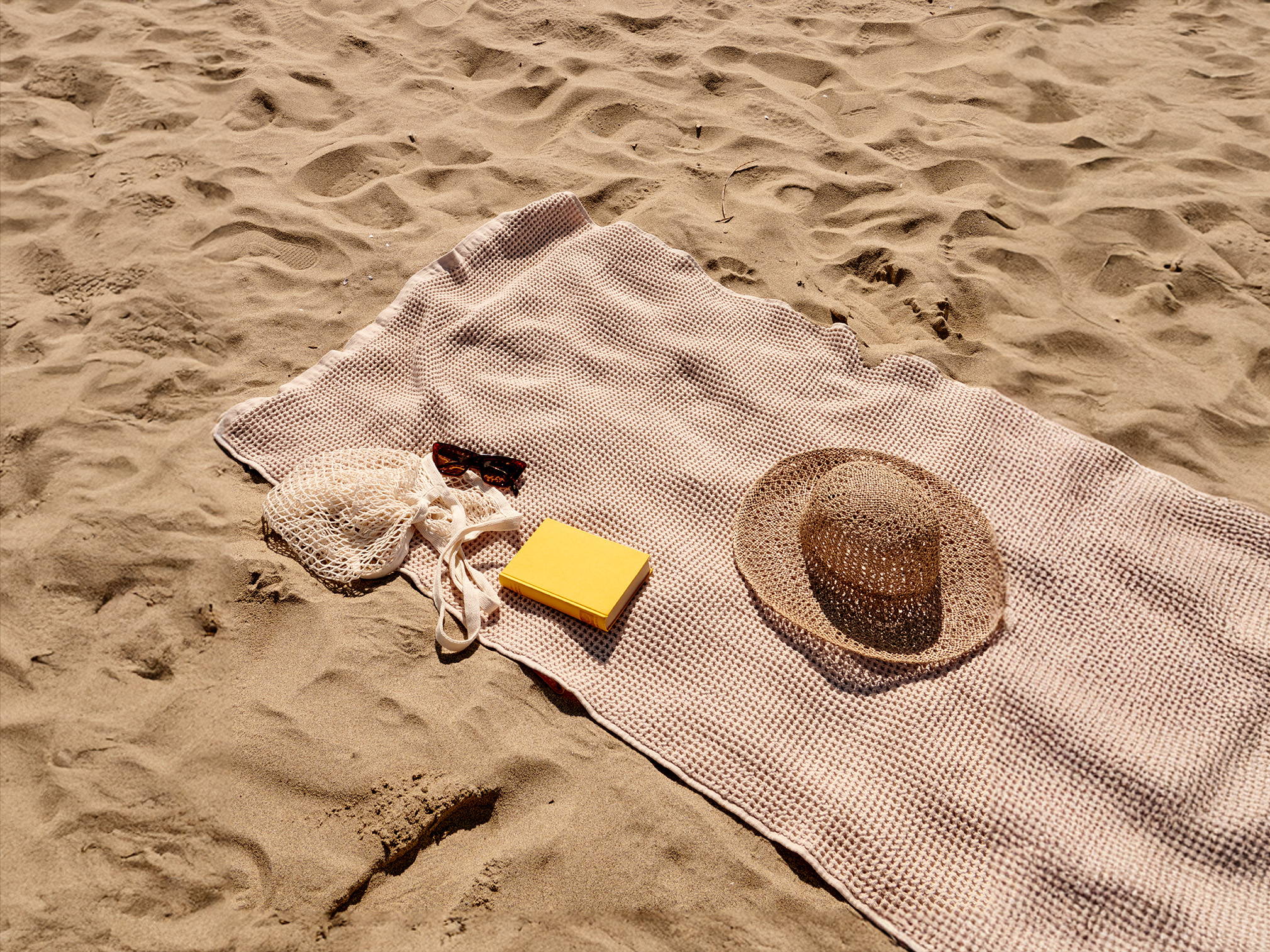 towel on the sand with sunglasses and a hat 