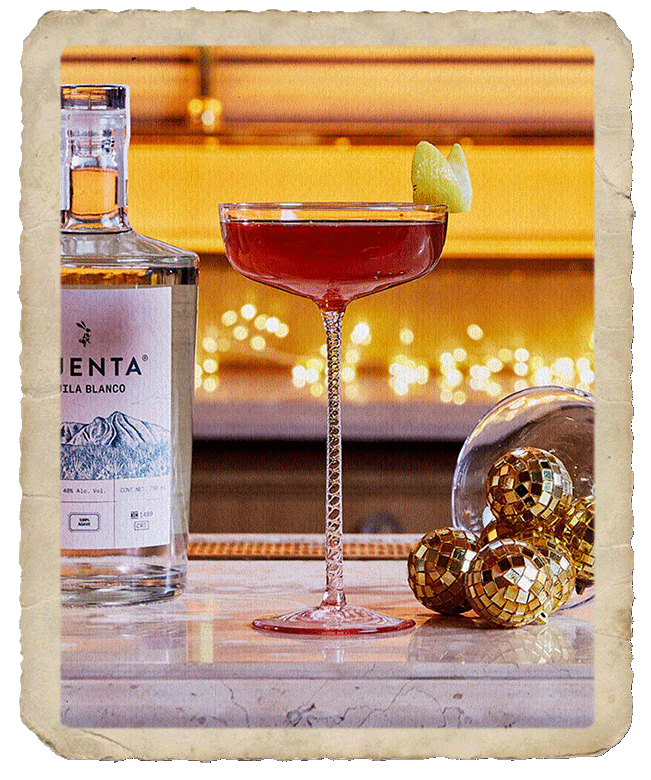 Tall glass with prepared cocktail, sided by a Mijenta Tequila Blanco bottle and christmas baubles.