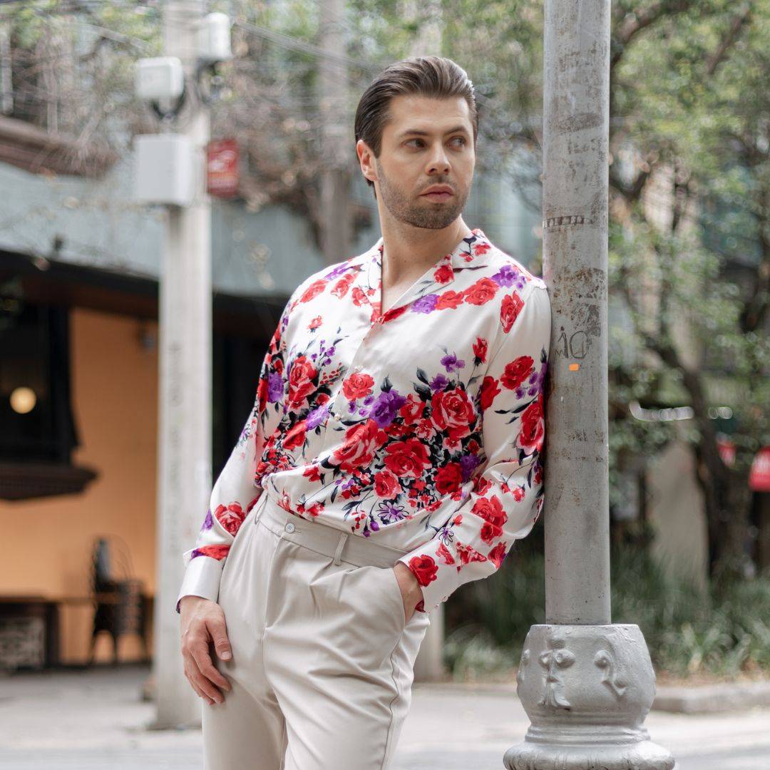 model leaning against a street post wearing white pants and a long sleeve white floral silk shirt from 1000 kingdoms