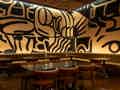 Stilvolles Restaurant-Interieur mit hellbraunen Lederbänken, dunklen Tischen und goldenen Pendelleuchten vor einem markanten abstrakten Wandgemälde.