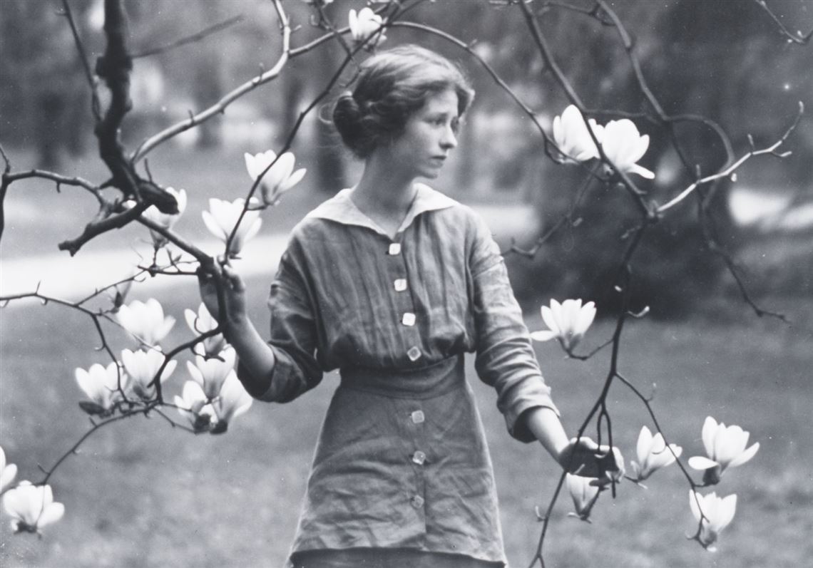 A black and white image of Edna in the outdoors holding a branch from a tree with white flowers.