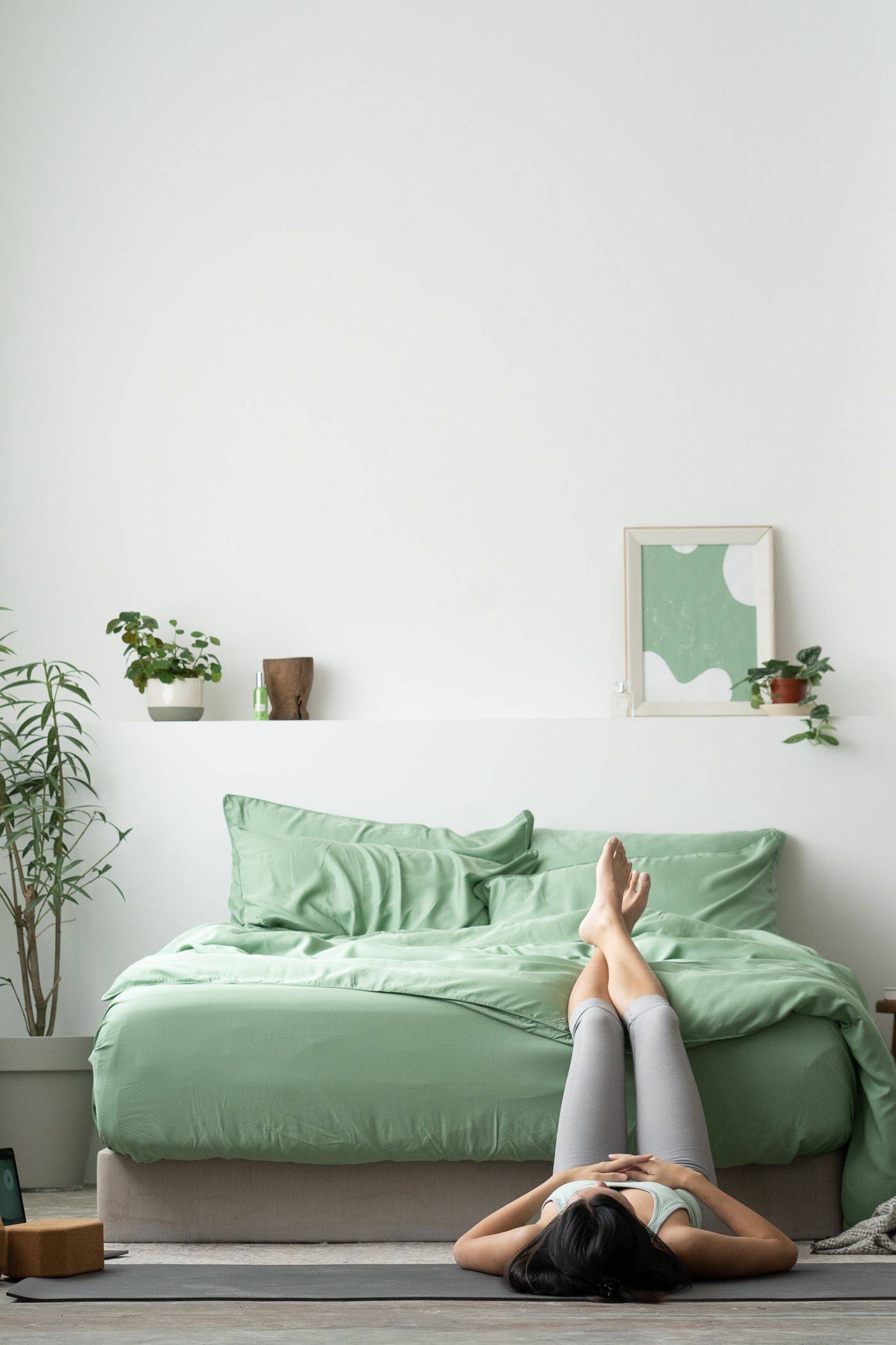 A girl laying on the floor with her legs up on the bed featuring Weavve's tencel lyocell bed sheets in green