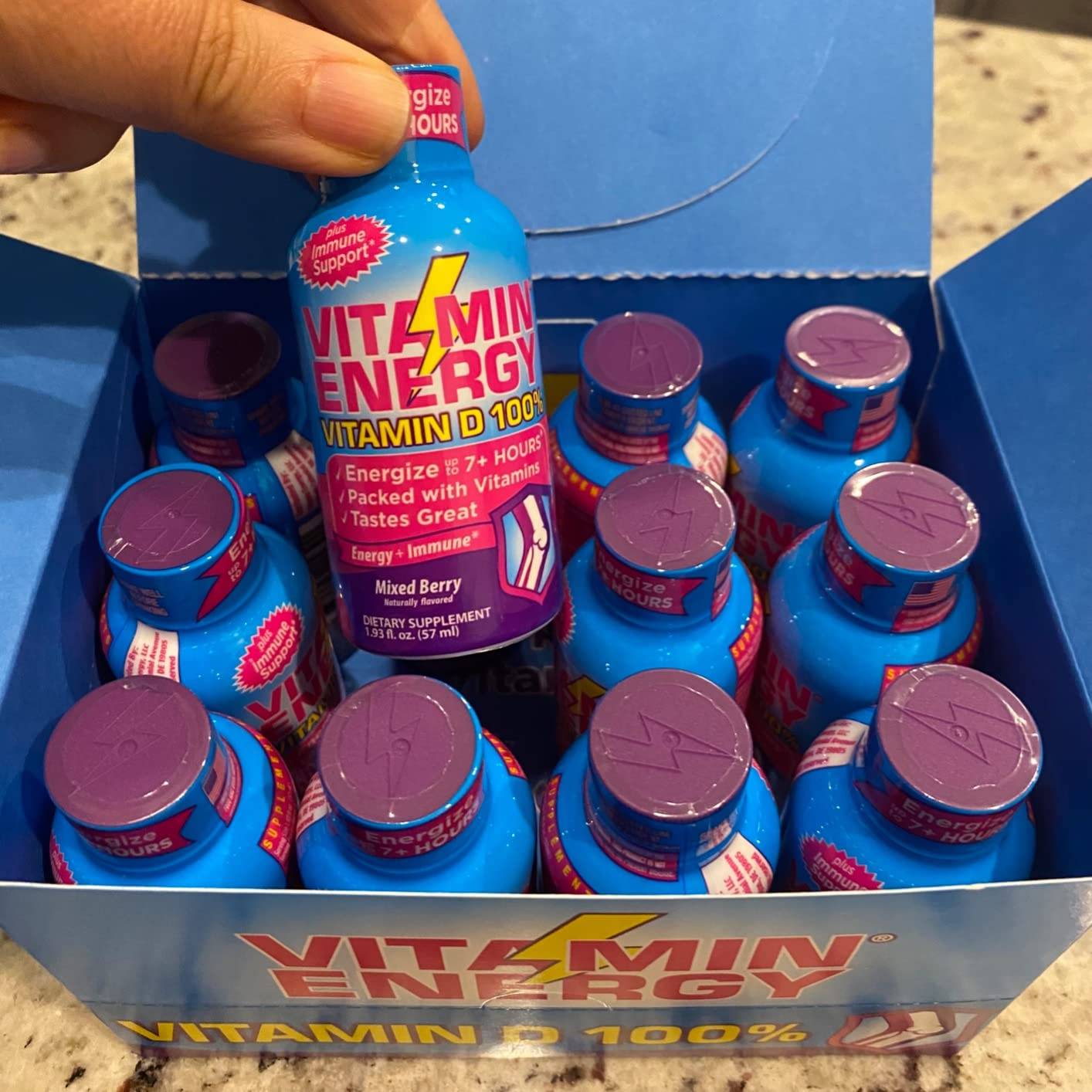 A blue box of vitamin energy shots with one being held up for display.