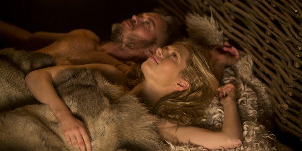 Ragnar and Lagertha Lothbrok laying down together on their bed and smiling looking to the cieling.
