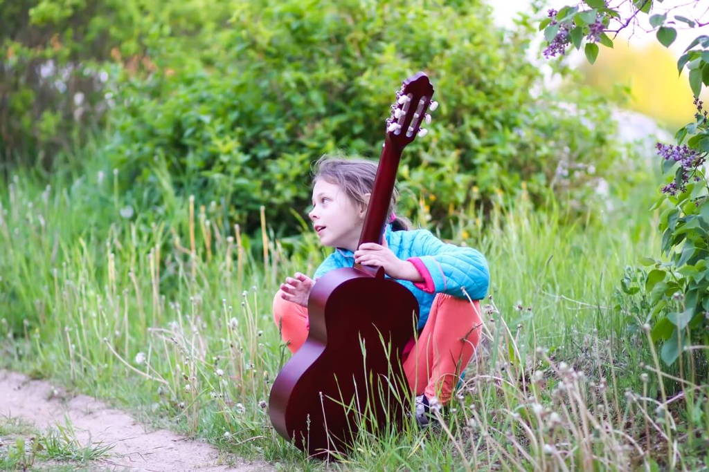 Child posing with an acoustic guitar in the forest.