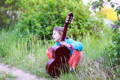 Child posing with an acoustic guitar in the forest.